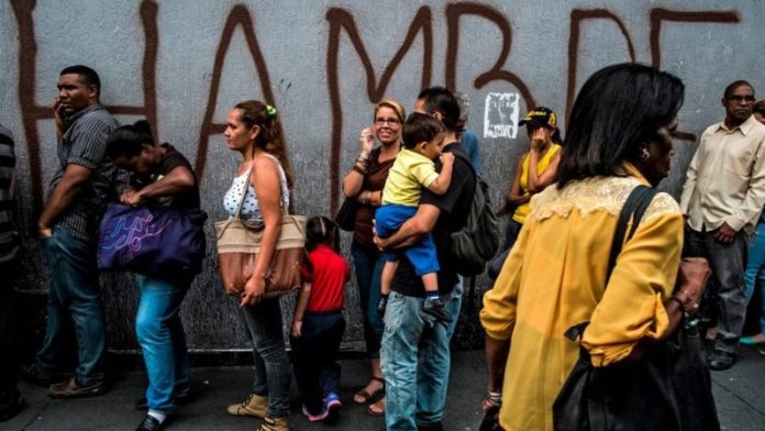 Crisis en Venezuela - personas en una cola y mural dice hambre